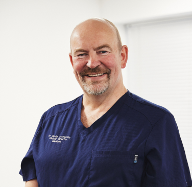 Dr David Eccleston smiling in blue medical scrubs at MediZen clinic.
