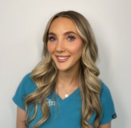 Young woman with long blonde hair smiling in a blue medical uniform.